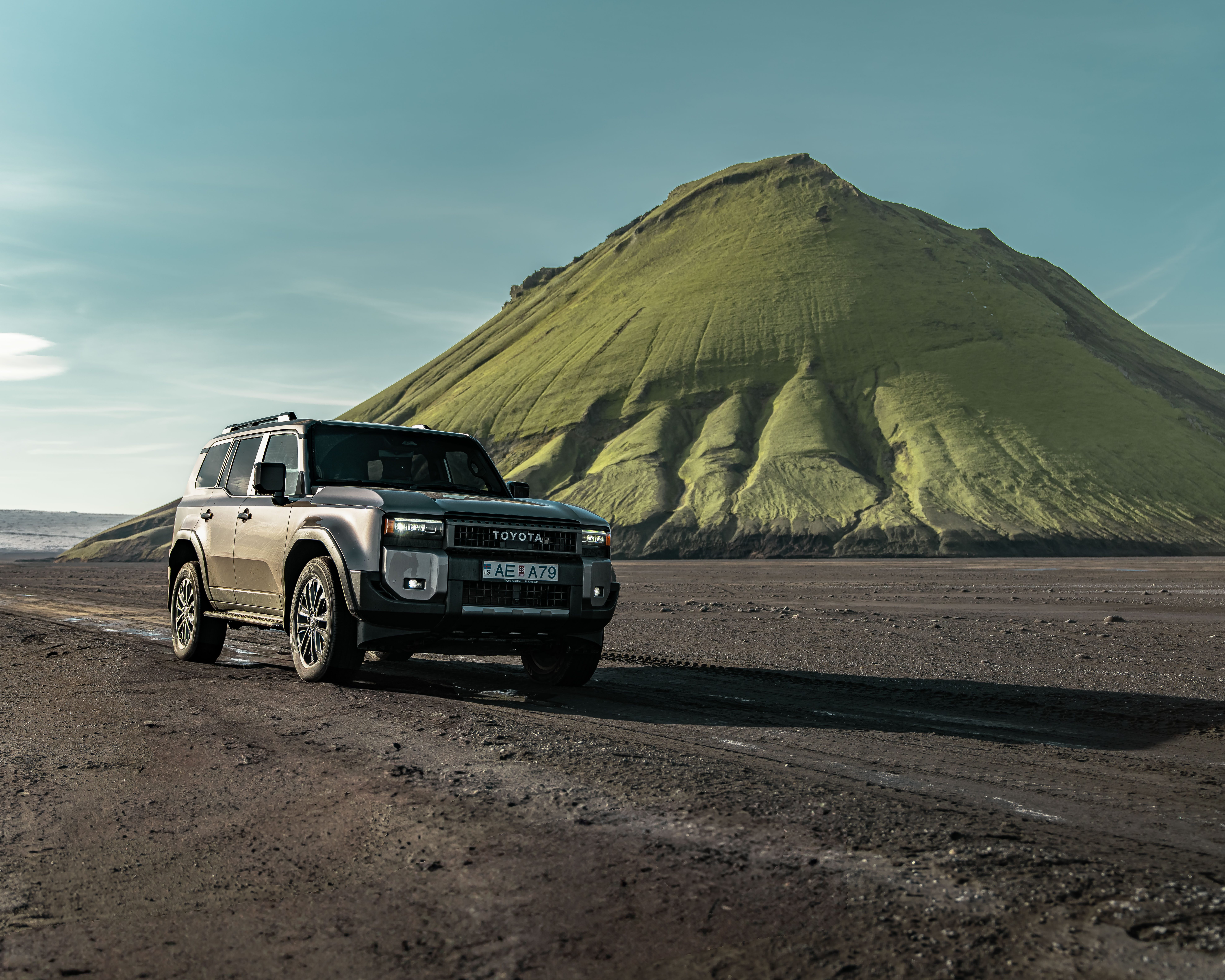 The new Toyota Land Cruiser 250 parked in front of the green Mælifell volcano on the F210 mountain road in Iceland.